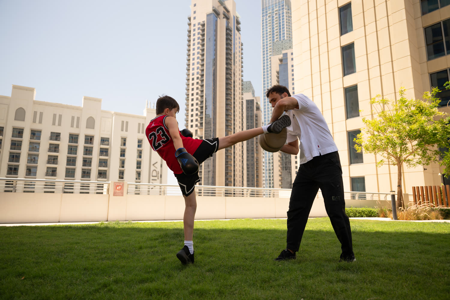 Young student landing a high kick on the pads with Illias, Dubai skyline behind